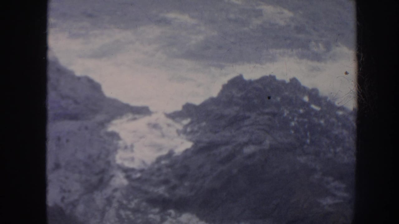 1961 Hawaii 8mm frame showing foamy waves striking jagged coastal rocks beneath an overcast sky.
