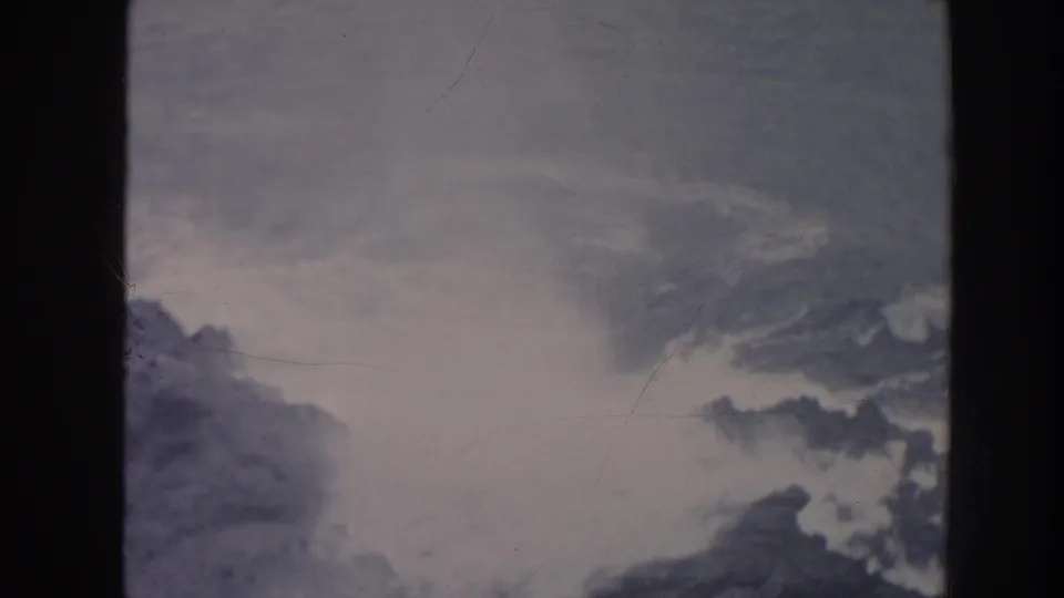 Foamy surf dominates the center of a 1961 Hawaii shoreline frame, with dark rocks at the edges and soft film fading.