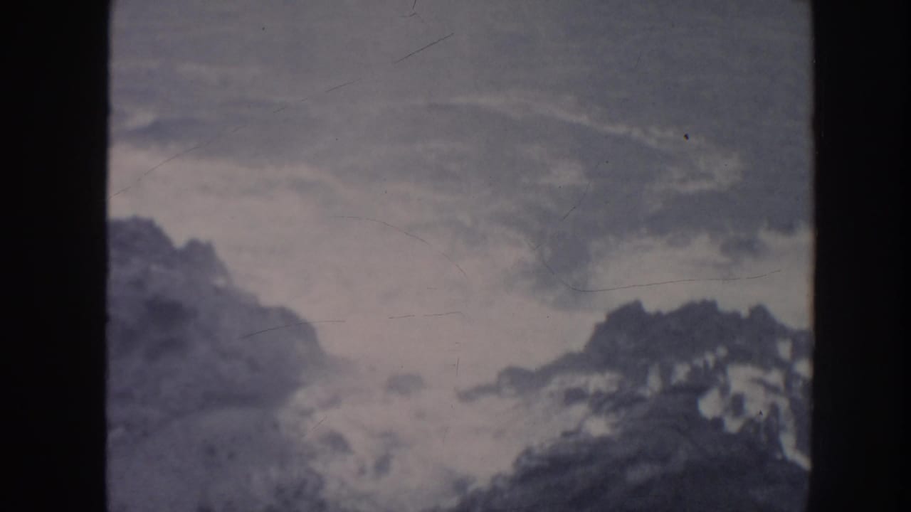 1961 Hawaii 8mm frame showing overcast sky and distant mountain forms viewed through dark vertical framing.