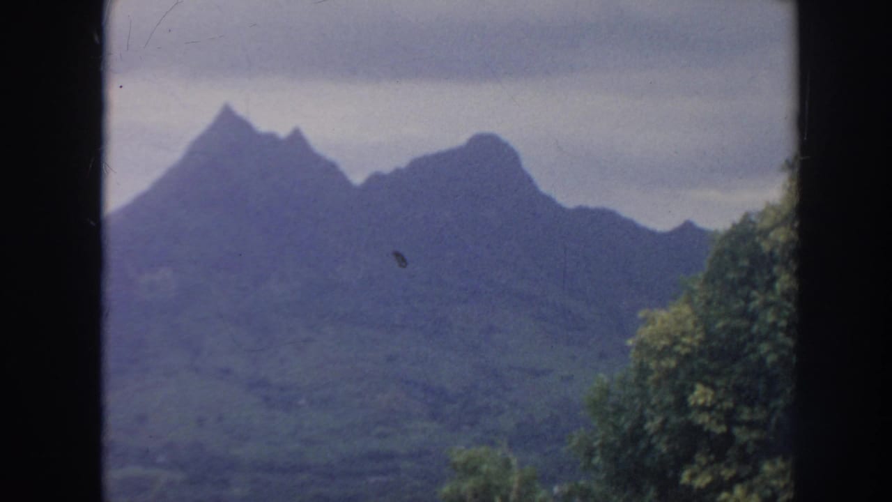 Jagged green mountain ridge under an overcast sky with trees at right.