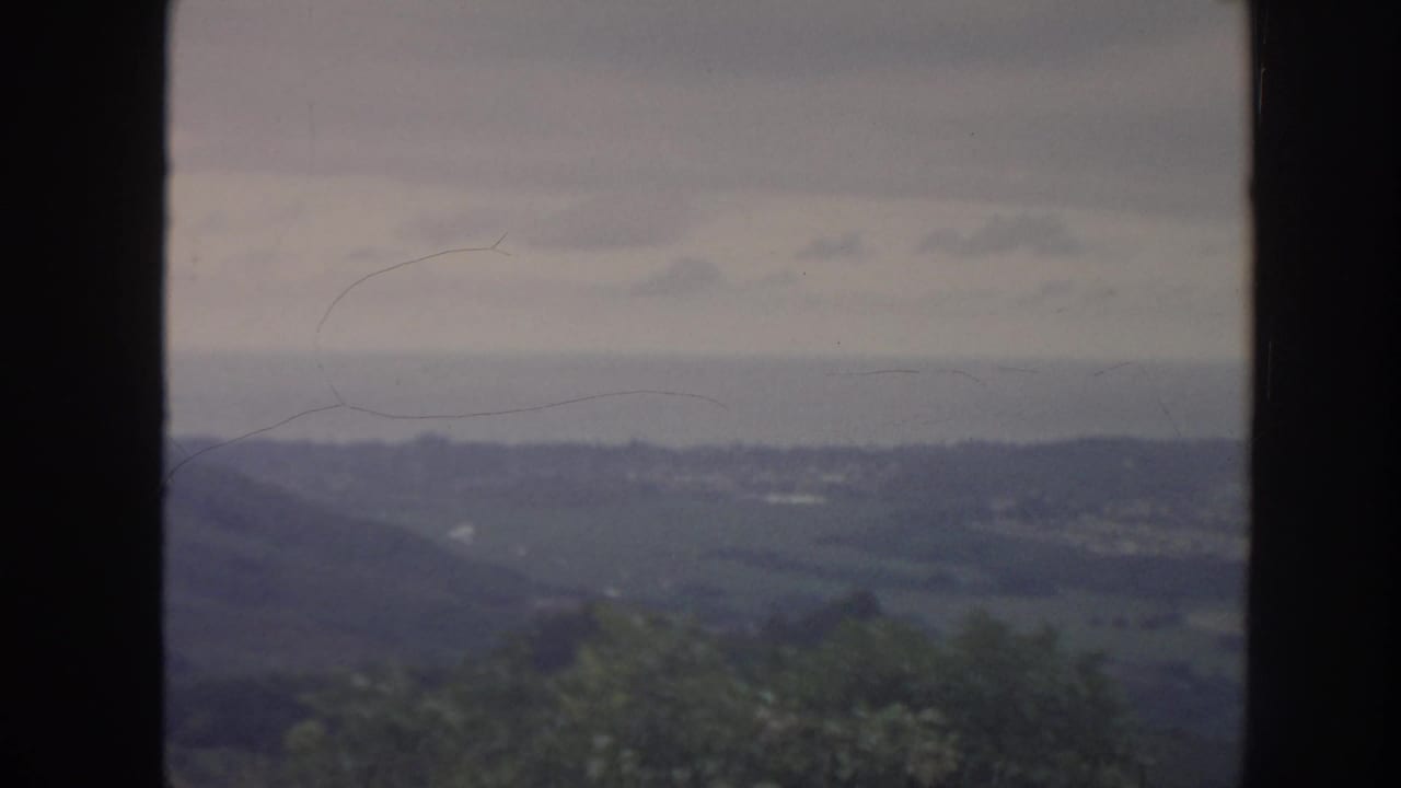 1961 Hawaii home-movie frame with rolling hills and valley greenery seen through a vertical window mullion.