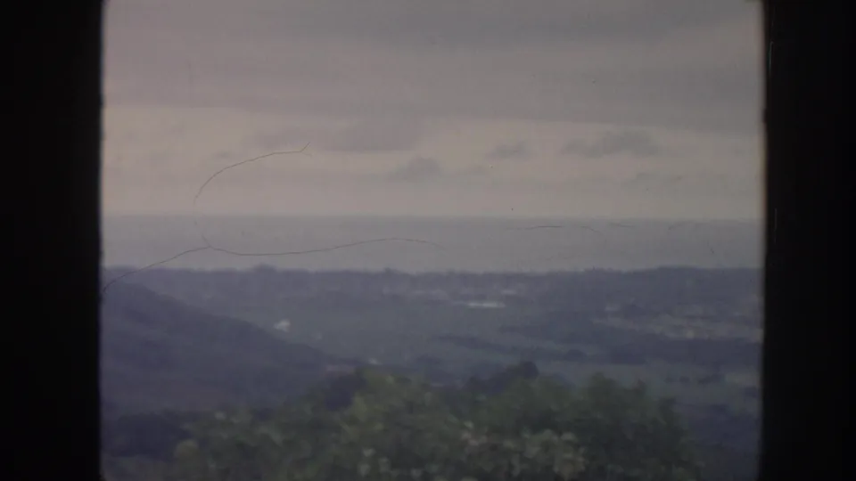 1961 Hawaii home-movie frame with rolling hills and valley greenery seen through a vertical window mullion.
