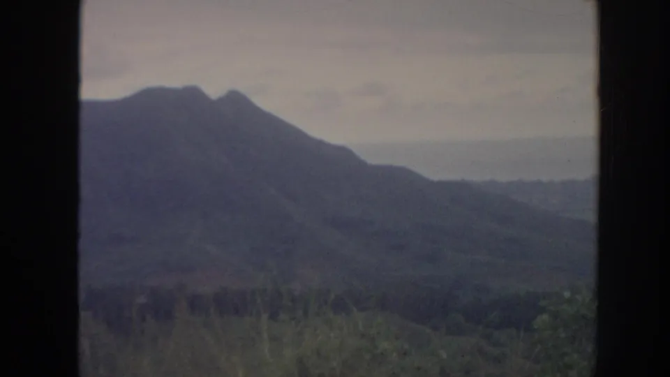 1961 Hawaii 8mm view of a dark mountain ridge, valley vegetation, and pale overcast sky through a window frame.