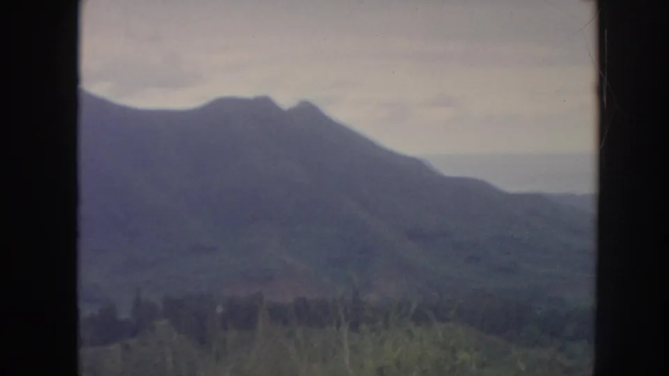 1961 Hawaii home-movie frame showing a mountain ridge and green valley foreground behind a dark window mullion.