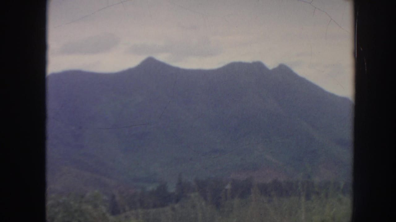 1961 Hawaii 8mm view of a dark-framed mountain ridge with forested lower slopes under an overcast sky.