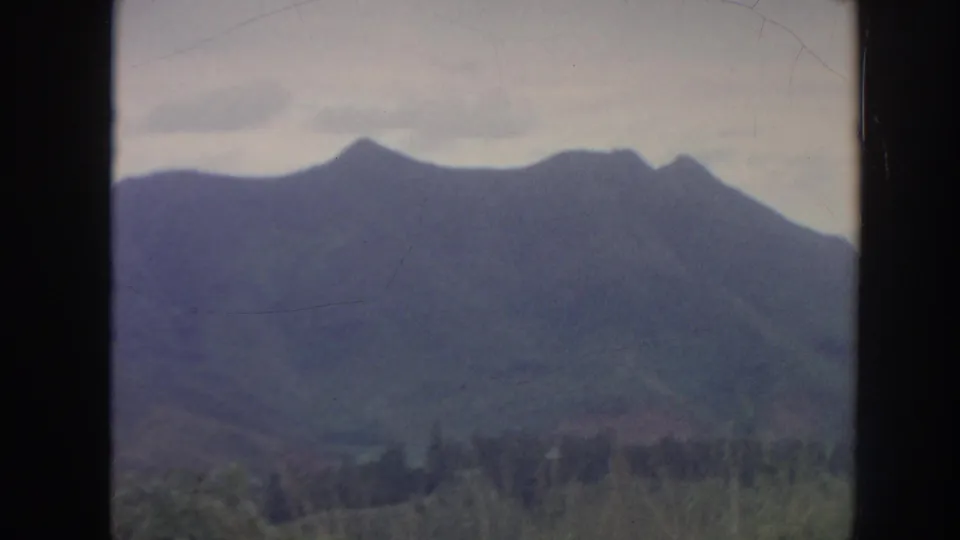 1961 Hawaii 8mm view of a dark-framed mountain ridge with forested lower slopes under an overcast sky.