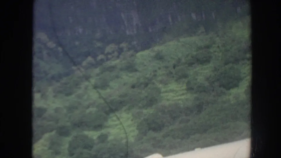 Forested Hawaiian mountainside in muted 8mm color, framed by a dark vertical edge and soft atmospheric haze.