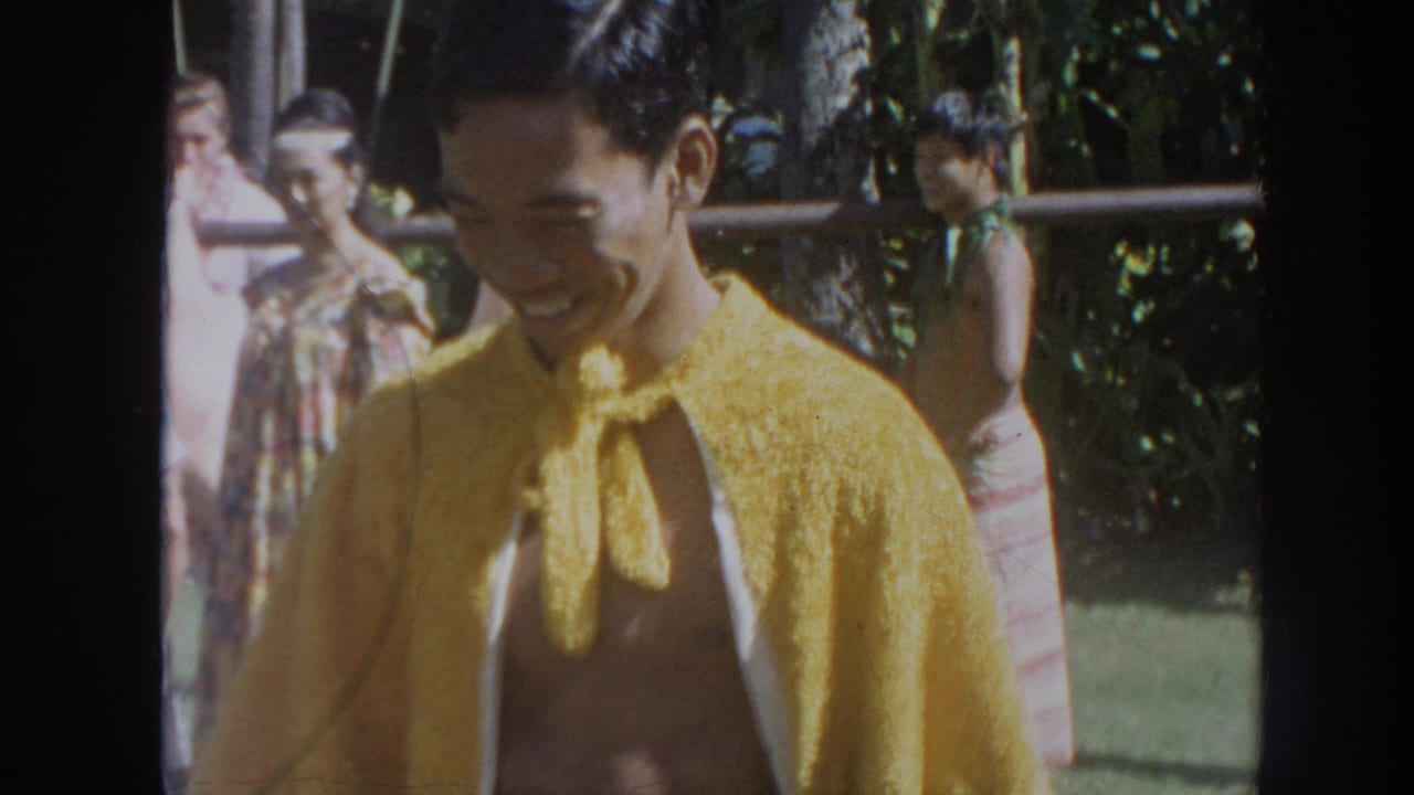Smiling man in a yellow cloak with other people behind him outdoors.