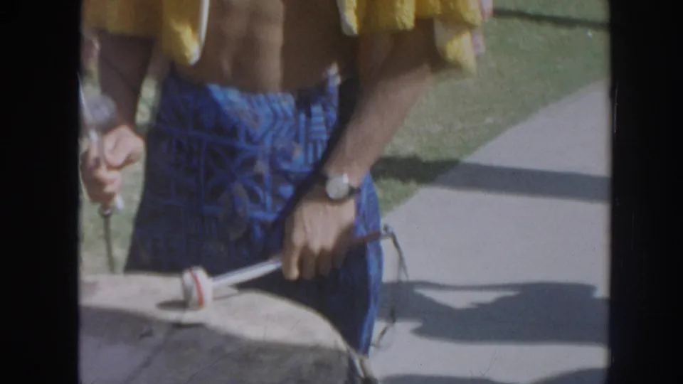 1961 Hawaii home-movie frame showing a close view of a drum mallet held near a large drum during the luau scene.