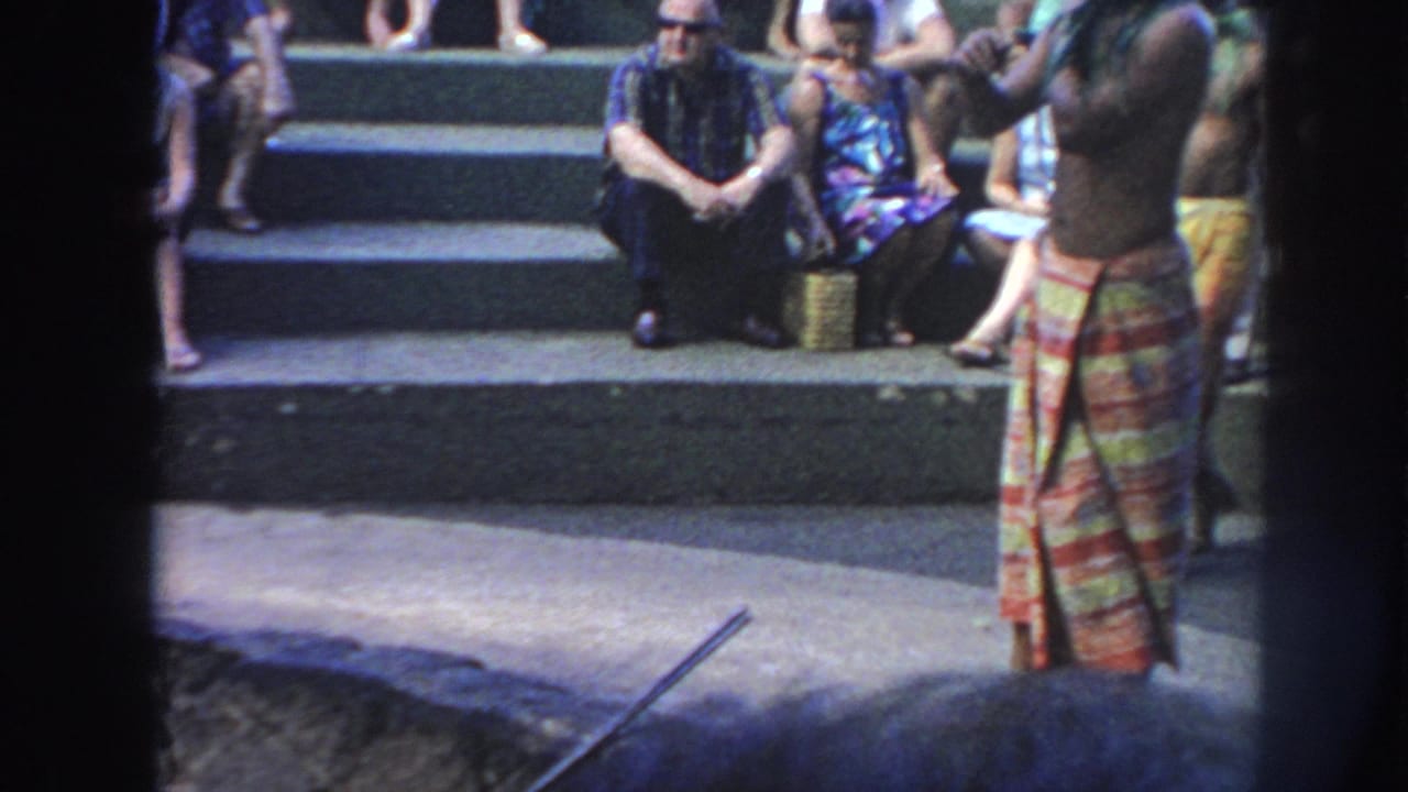 1961 Hawaii visitor footage shows a shirtless man in a colorful wrap standing near the edge of a deep fire pit with an audience behind him.