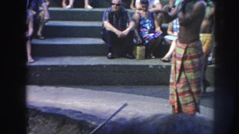 1961 Hawaii visitor footage shows a shirtless man in a colorful wrap standing near the edge of a deep fire pit with an audience behind him.