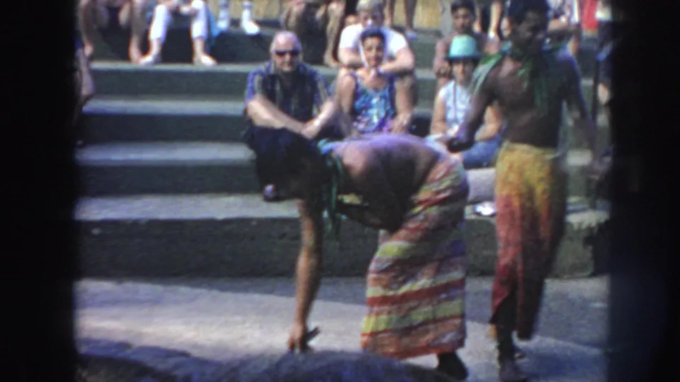 1961 Hawaii 8mm footage shows men in bright patterned wraps using long tools around a deep fire pit before a seated audience.