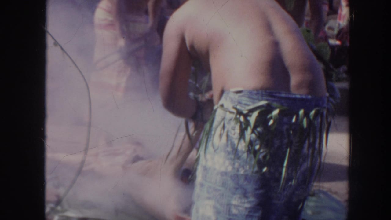 1961 Hawaii home-movie frame showing a shirtless performer from behind near smoke during a Polynesian cultural performance.