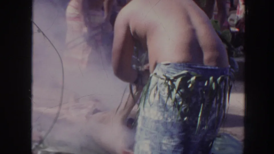 1961 Hawaii home-movie frame showing a shirtless performer from behind near smoke during a Polynesian cultural performance.