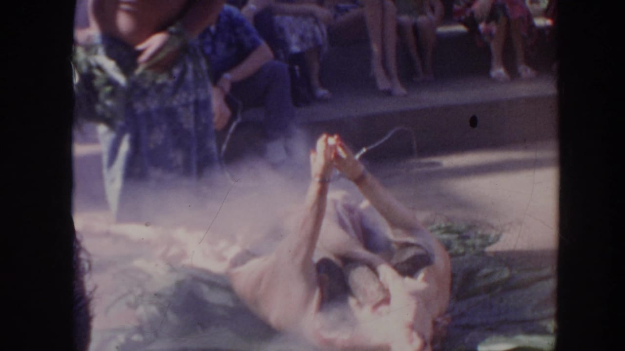 Man bends near a smoking whole pig while spectators sit behind the roasting area.