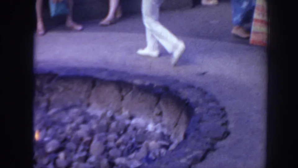 1961 Hawaii 8mm frame showing performers or participants walking near a stone-lined pit during an outdoor ceremony.