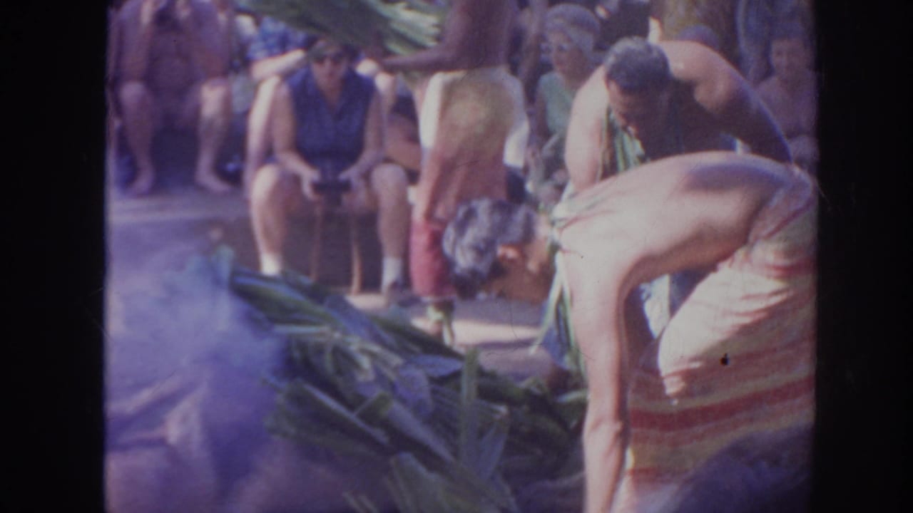 Performers bend over a pile of banana leaves with spectators behind them.