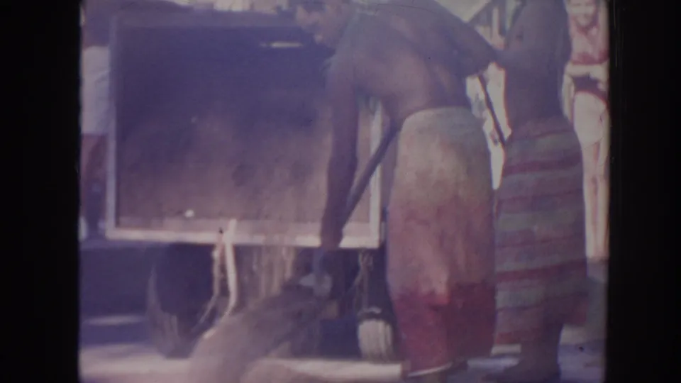 A 1961 Hawaii frame shows men around a large wooden box or truck bed, with one figure holding a shovel nearby.