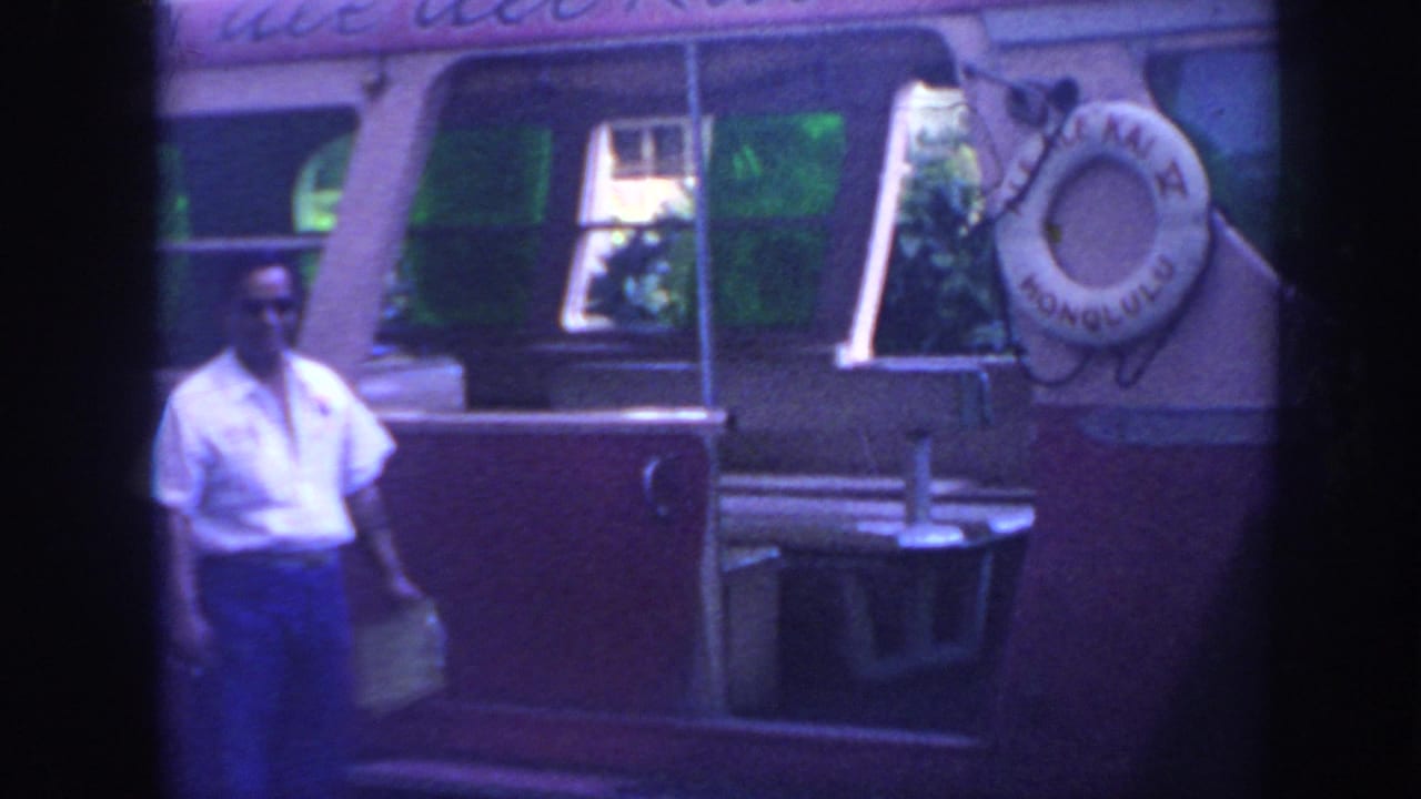 Pink-and-white bus beside a man in a white shirt, with a life preserver mounted on the side.