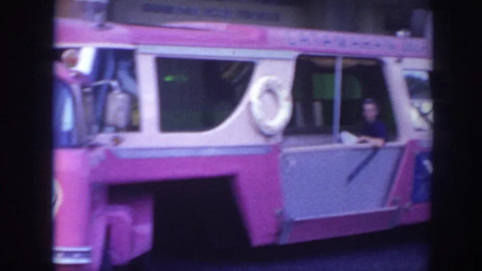 1961 Hawaii 8mm frame showing the side of the pink-and-white bus with a life preserver and a person visible at an open window.