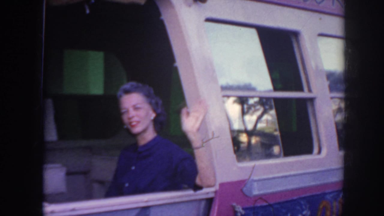A smiling woman waves beside the open window of a pink-and-white bus in supported 1961 Hawaii travel footage.