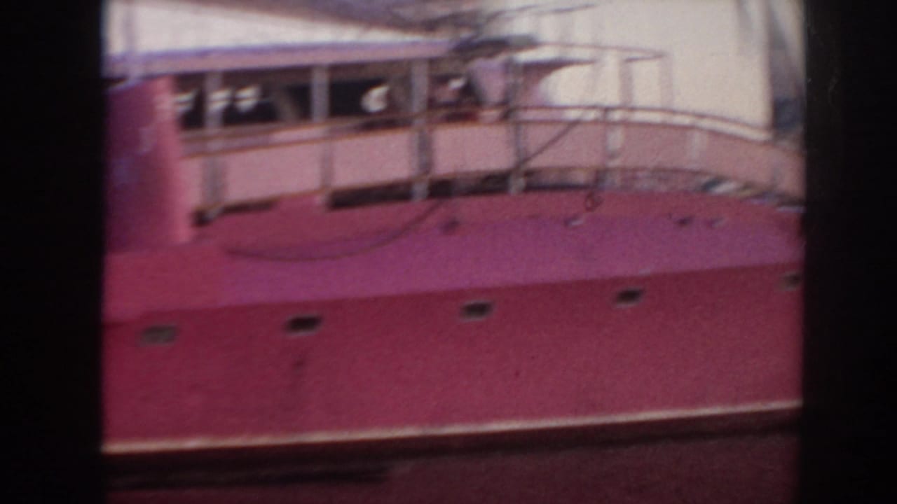 Pink-hulled boat seen close from the side, with deck railings and cabin structure above.
