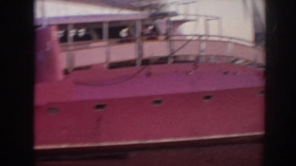 1961 Hawaii 8mm frame showing the side of a pink-hulled boat at a pier, with railings and cabin details visible.