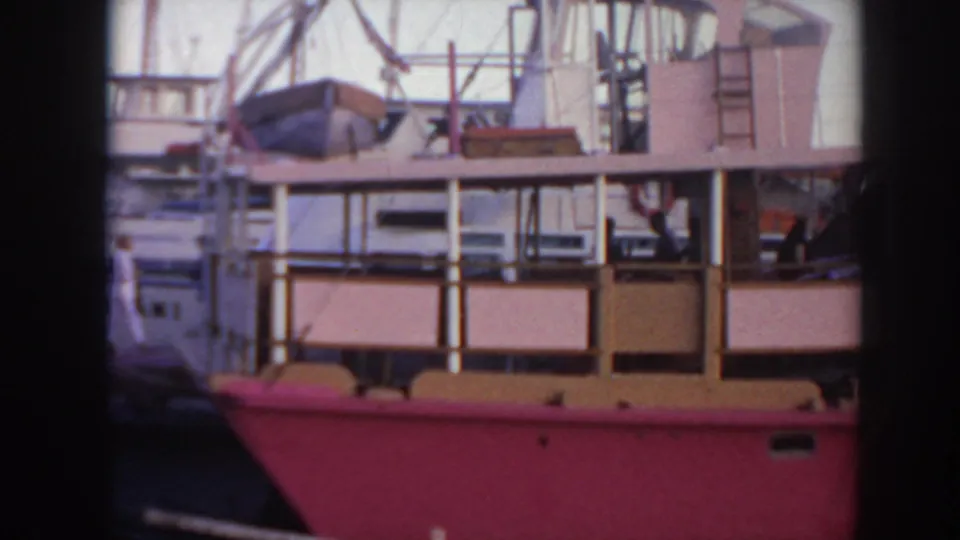 1961 Hawaii 8mm frame showing the pink boat from the side, including deck railings, equipment, and distant people aboard.