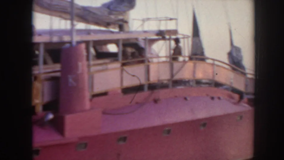 1961 Hawaii home-movie frame showing a red-hulled boat with railings and upper deck details in a harbor setting.