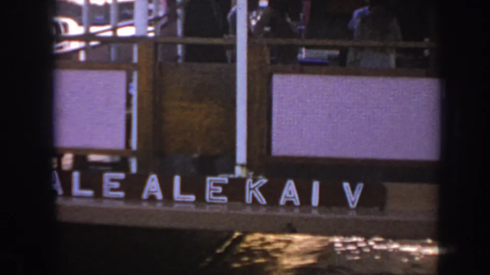 Home-movie frame from 1961 Hawaii showing the ALEKAI V name on a vessel side with deck railings and figures partly visible above.