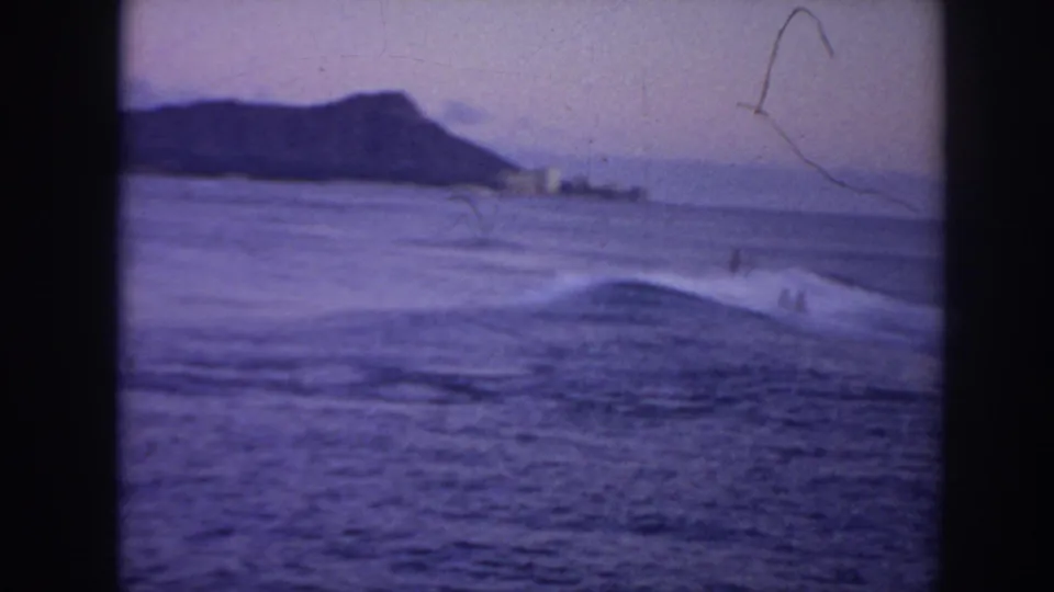 1961 Hawaii 8mm frame with Diamond Head in the distance and surfers scattered across low surf.