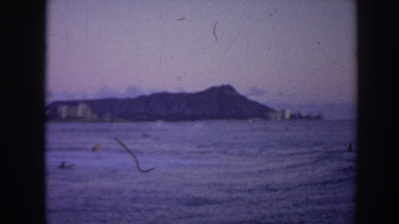 Distant Diamond Head beyond ocean water with small figures on the waves.