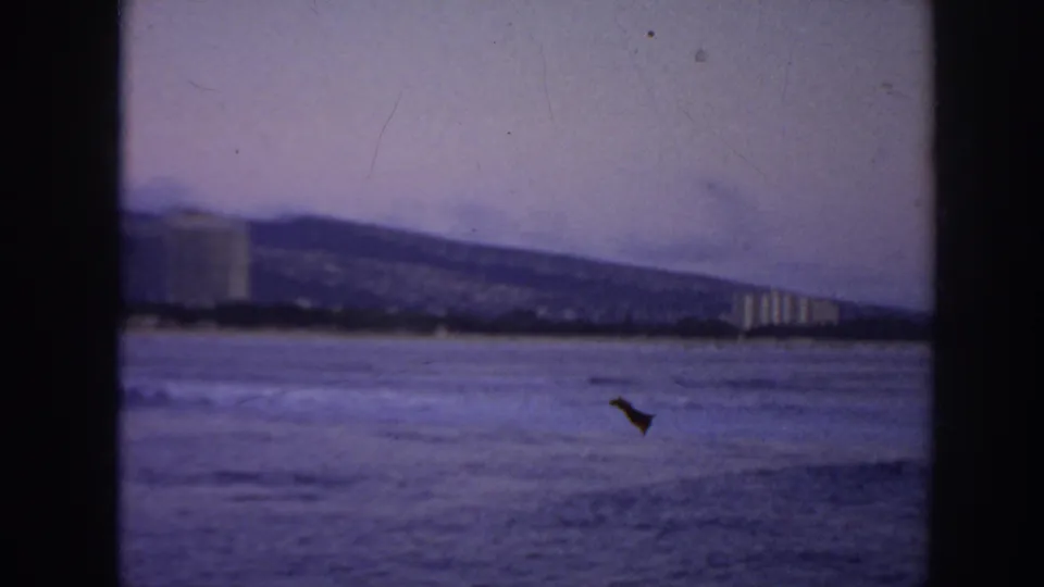 1961 Hawaii home-movie view of ocean, distant shoreline buildings, and a hillside behind the coast.