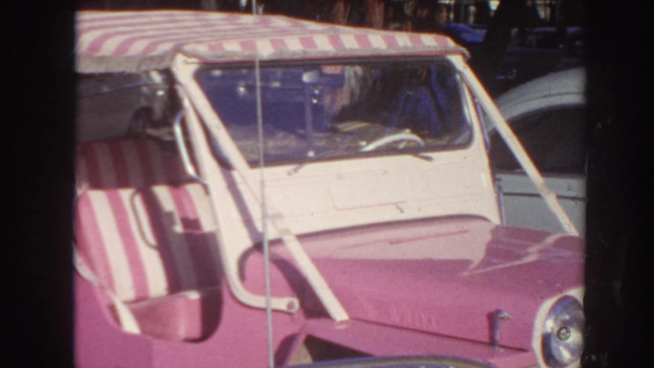 Pink and white convertible car with striped canopy parked among other vehicles.