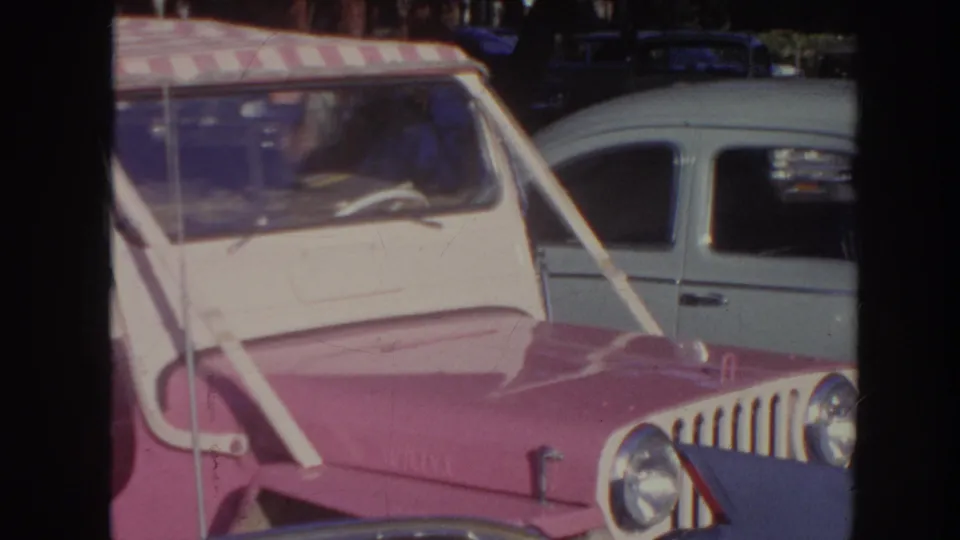 Close 1961 Hawaii home-movie view of the pink canopy car's front end beside a light-colored parked car.