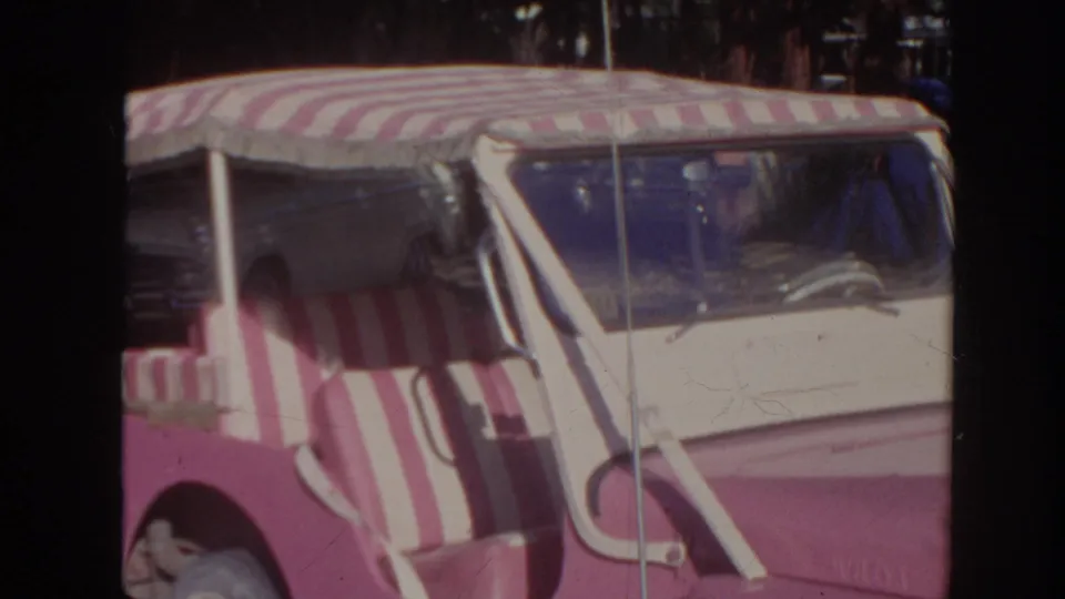 1961 Hawaii home-movie frame showing the pink-and-white striped canopy car from the side and front in a parking area.