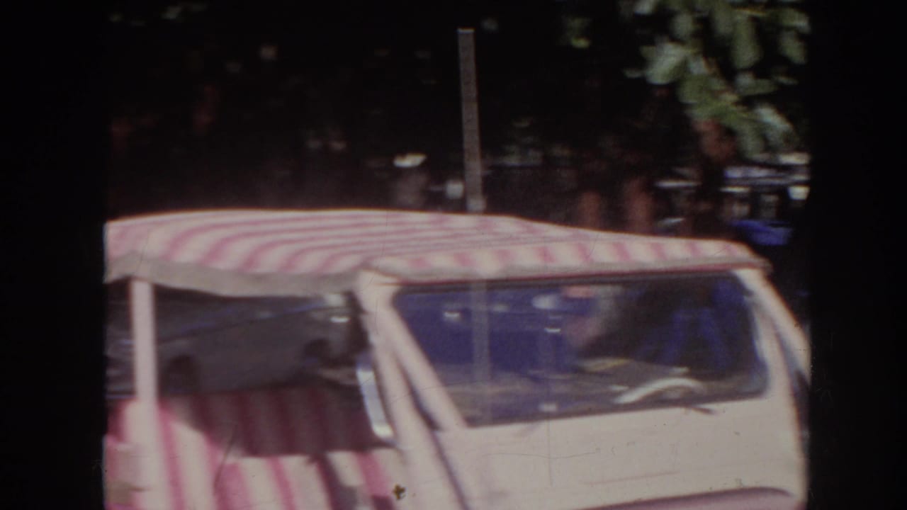 1961 Hawaii 8mm frame showing the upper portion of a pink open vehicle with a red-and-white striped canopy in a parking area.