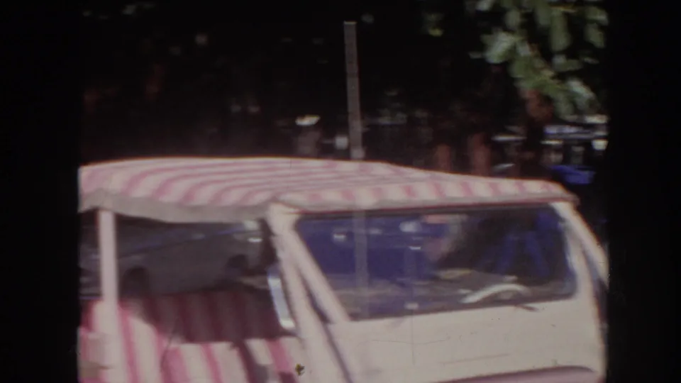 1961 Hawaii 8mm frame showing the upper portion of a pink open vehicle with a red-and-white striped canopy in a parking area.