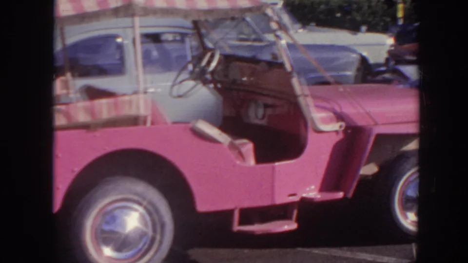 1961 Hawaii 8mm still with a close side view of the pink open vehicle, striped canopy edge, steering wheel, and chrome wheel cover.