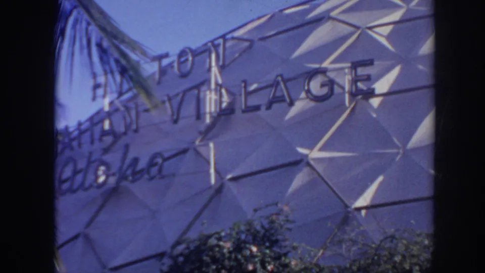 1961 Honolulu resort frame with Hilton Village signage, palm fronds, shrubs, and a white geometric dome surface.