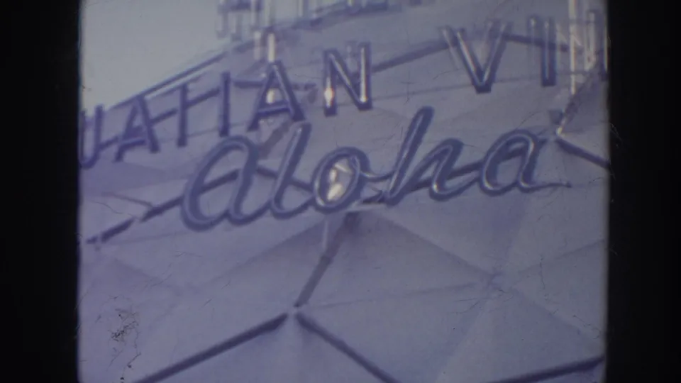 Cropped 1961 Hawaii frame of Hawaiian Village aloha signage across a faceted hotel exterior wall.