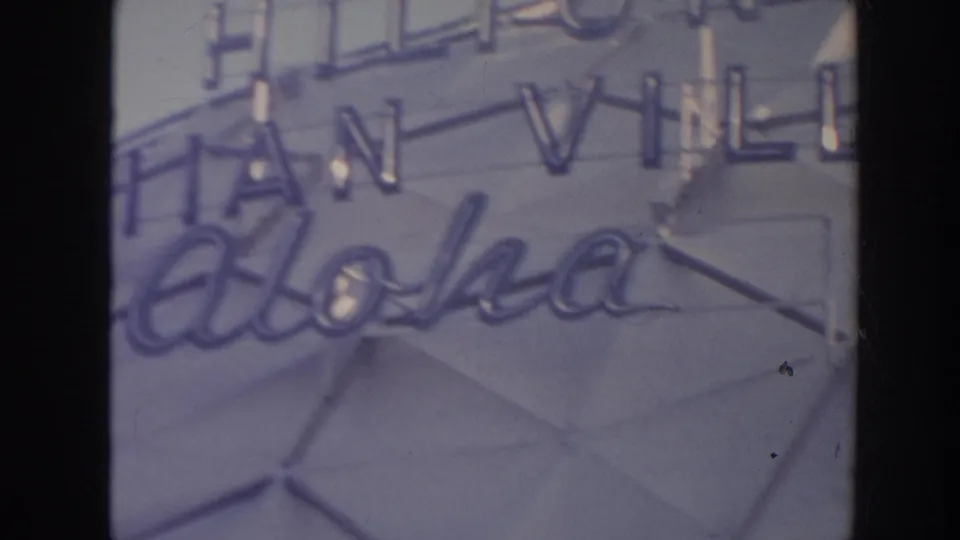 Soft 8mm frame from Hawaii showing the aloha script and partial Hawaiian Village sign on a geometric facade.