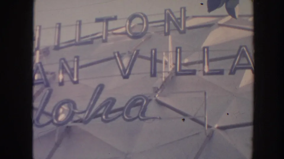 Hilton Hawaiian Village sign in Hawaii, with aloha script and mid-century geometric wall detail visible.