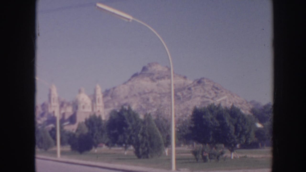 Mountain view with a curved streetlamp, trees, lawn, and a distant church-like structure.