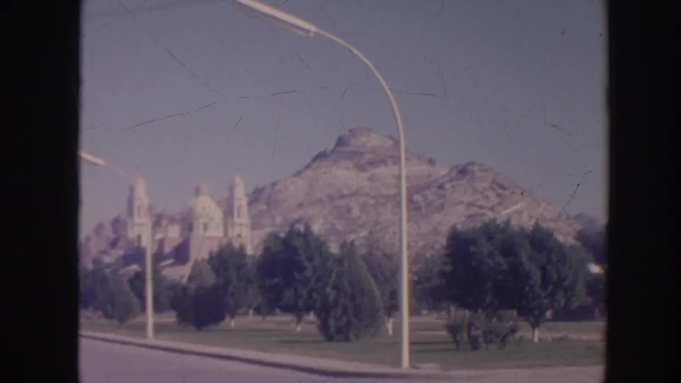 1961 Hawaii home-movie view of a mountain-backed landscape with trees, roadway, streetlamp, and a distant church-like structure.