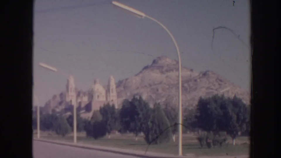 1961 Hawaii travel frame showing landscaped grounds, a curved streetlamp, a distant church-like structure, and a rocky mountain backdrop.