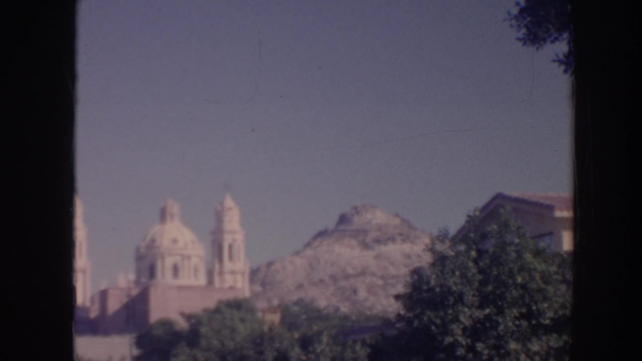 1961 Hawaii 8mm frame showing a distant domed church with bell towers, trees, a rugged hill, and a curved streetlight at the edge.