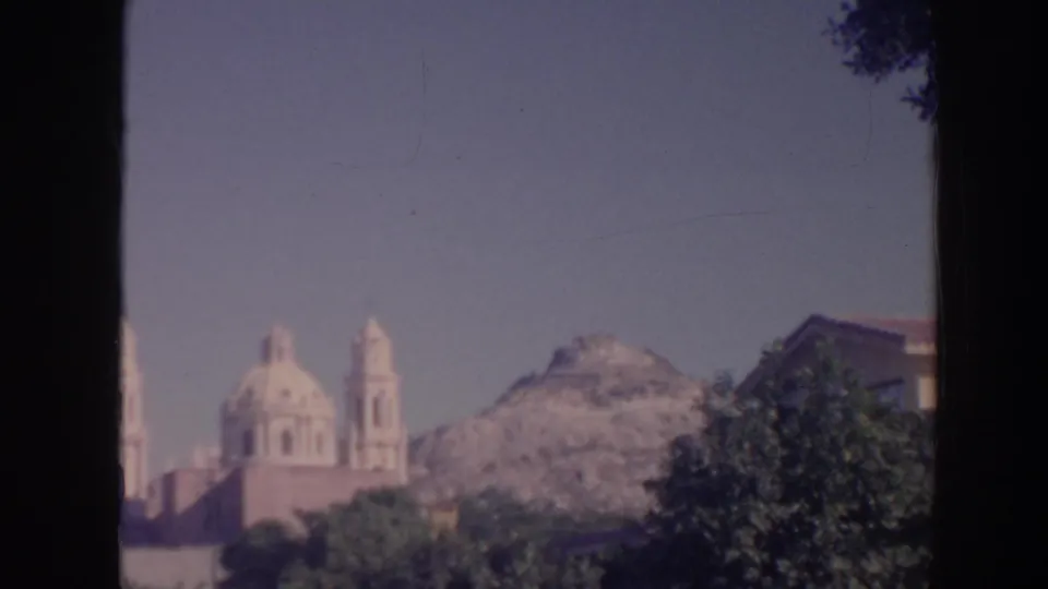 1961 Hawaii 8mm frame showing a distant domed church with bell towers, trees, a rugged hill, and a curved streetlight at the edge.