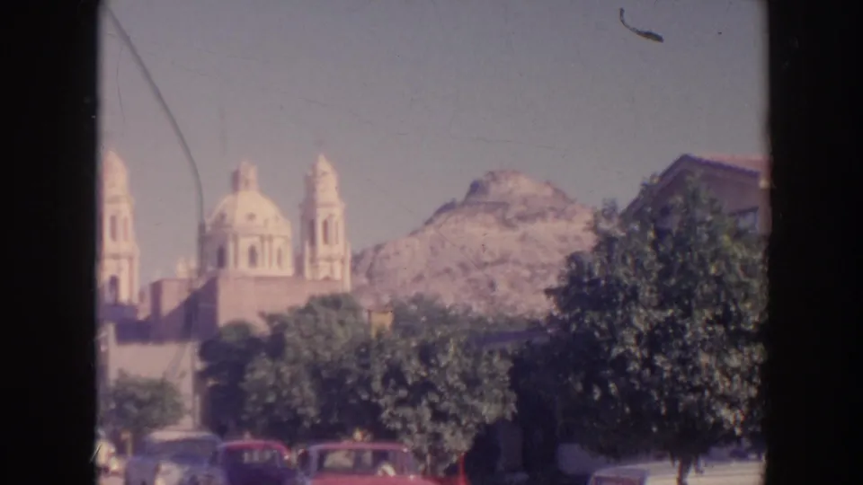 1961 8mm travel frame with a domed landmark, rocky hillside, trees, and mid-century cars visible in the foreground.