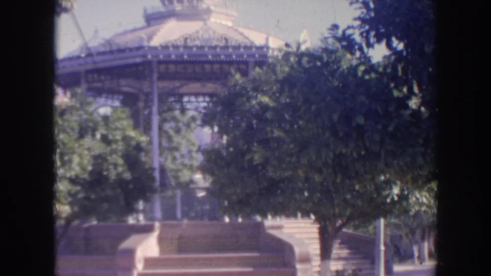 1961 Hawaii 8mm frame showing the gazebo more to the rear, partly screened by dark foliage, with a low wall and paved or stepped foreground.